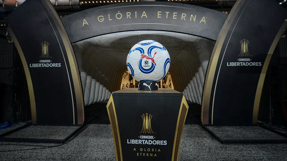 Bola da CONMEBOL Libertadores™ com banner “a glória eterna” ao fundo. 