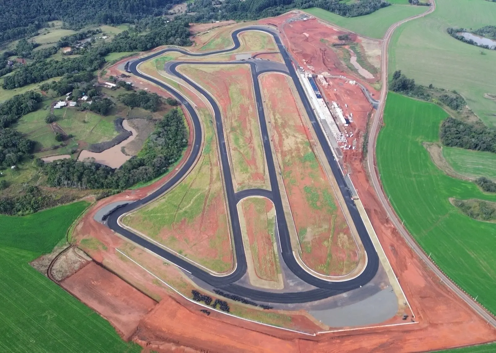 Vista aérea do Autódromo Internacional de Chapecó, mostrando o traçado asfaltado com longas retas, curvas fechadas e sequências sinuosas, cercado por áreas verdes e terrenos de solo avermelhado.