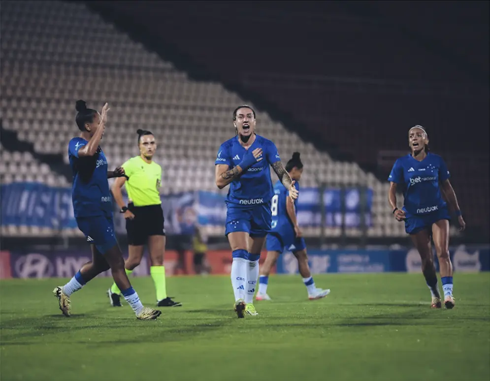 Jogadoras de futebol do Cruzeiro comemorando um gol dentro do campo. 