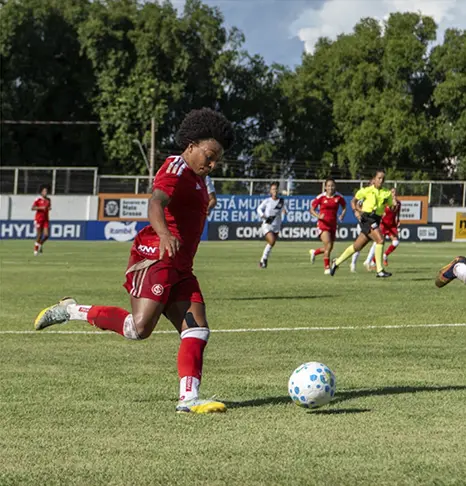 Jogadora de futebol do Internacional se preparando para jogar a bola contra o gol da Ponte Preta. 