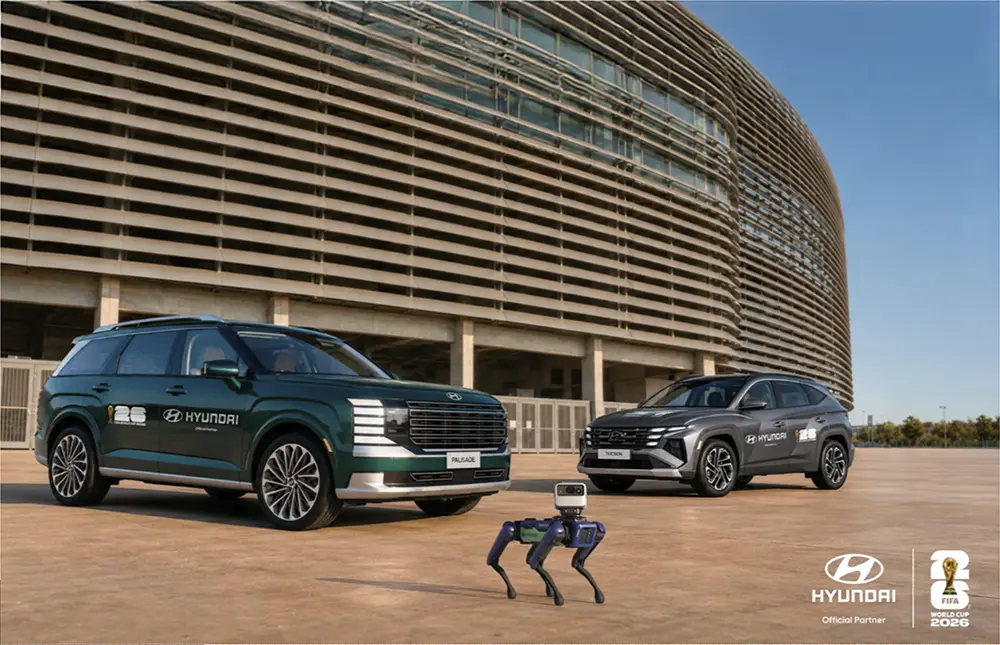 Robô Spot da Hyundai junto com o IONIQ 9 e o TUCSON híbrido no estacionamento de um estádio de futebol.