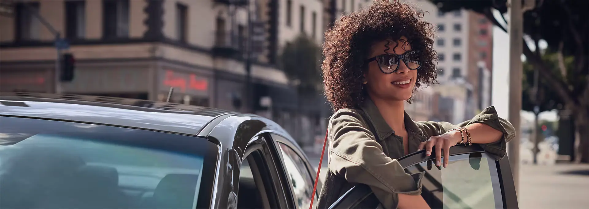 Mulher apoiada na porta de um carro estacionado na rua durante o dia.