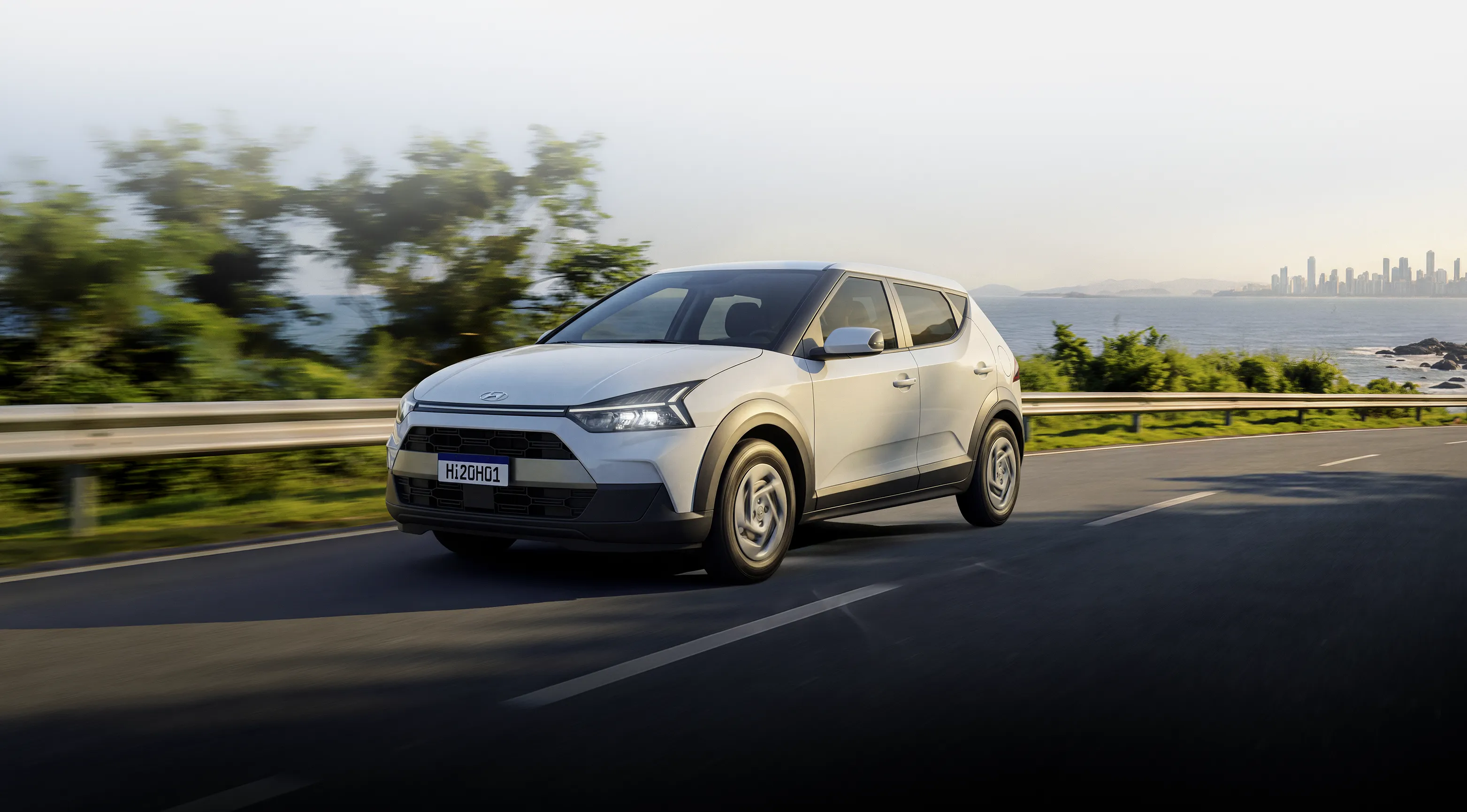 Novo Hyundai i20 na cor branca em alta velocidade na estrada com floresta ao fundo durante o dia.
