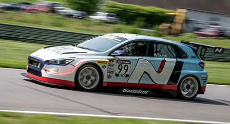 Modelo Hyundai i30 Rally N Line na cor azul em alta velocidade em uma pista de corrida durante o dia.