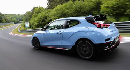 Modelo Hyundai Veloster N Line na cor azul em alta velocidade numa pista de corrida durante o dia.
