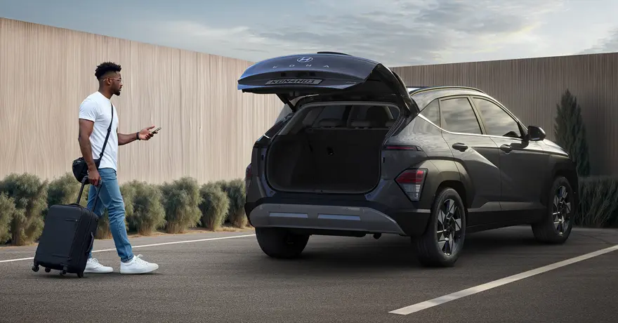 Porta-malas do KONA Híbrido levantado com homem segurando uma mala se aproximando.