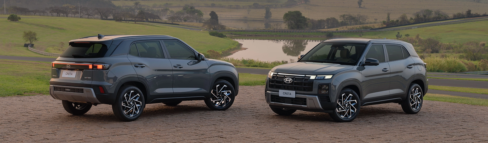Dois modelos do Hyundai CRETA estacionados em uma estrada durante o dia com lagoa de fundo .