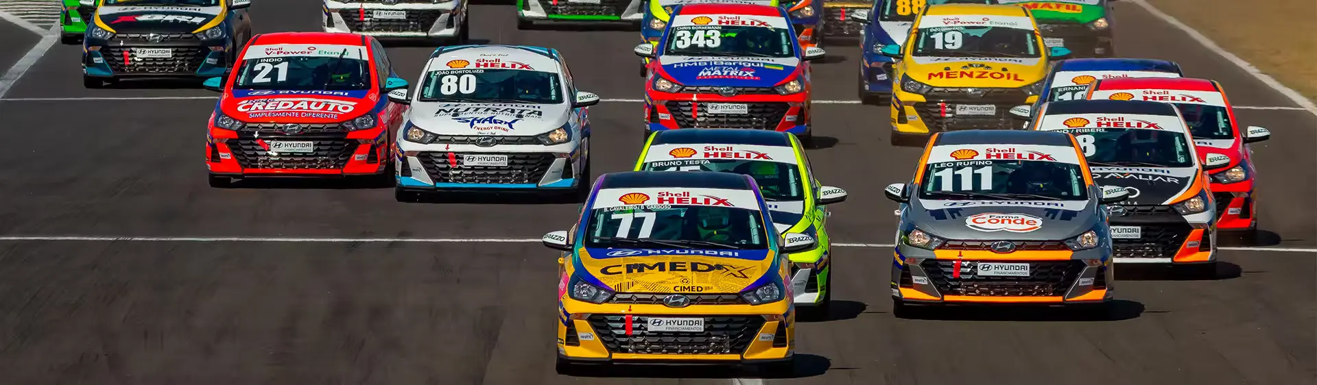 Modelos do HB20 de corrida após a largada em uma pista de corrida durante o dia.