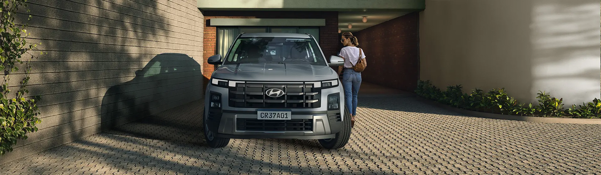 Modelo CRETA Comfort na cor cinza estacionado em uma casa durante o dia com mulher caminhando ao lado.