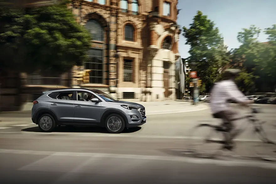 Modelo Tucson na cor cinza em alta velocidade na rua durante o dia com bicicleta em sua frente.