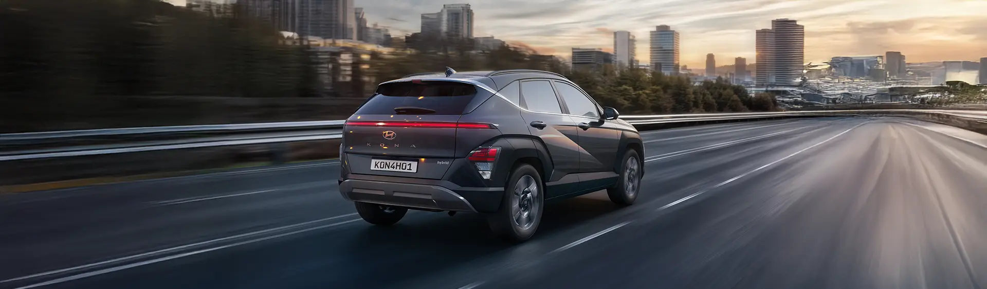 Visão traseira do KONA Híbrido na cor cinza em alta velocidade na estrada.