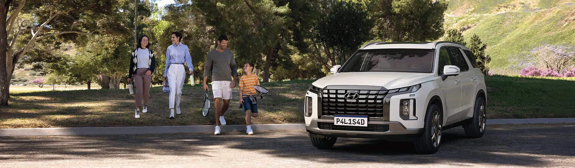 PALISADE branco estacionado em um parque em dia ensolarado com família ao lado. 